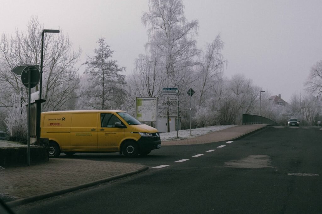 A yellow DHL delivery van parked on a frosty winter street corner, showcasing urban logistics.